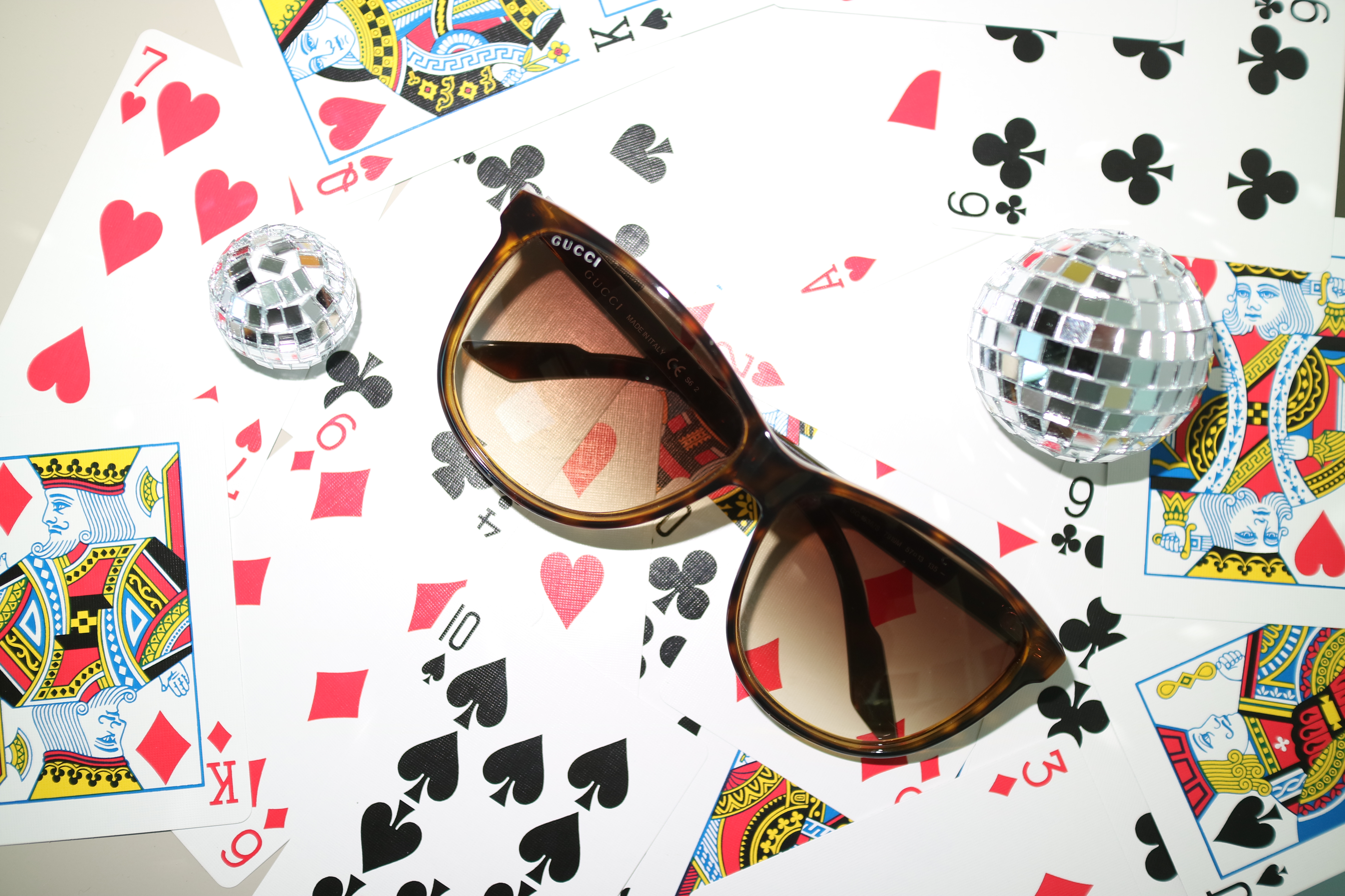 Tortoiseshell Gucci sunglasses and mirrored disco balls arranged over oversized playing cards.